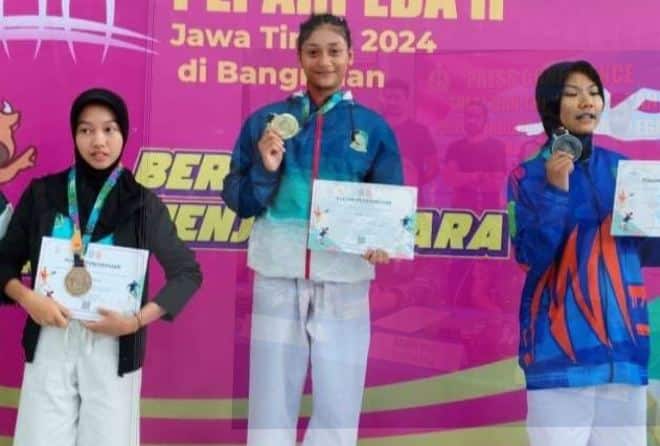 Dua atlet kempo dari Banyuwangi, Andini Masayu dan Yetania Vita Zabrina, sedang memegang medali emas yang diraihnya di Popda Jatim 2024. Mereka terlihat tersenyum bahagia dan bangga.